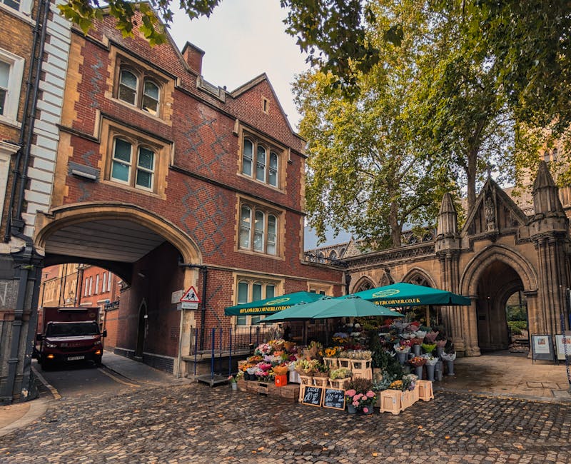 A vibrant flower stall situated on a cobblestone street beneath a large green umbrella displaying the domain name bowesparkflorist.co.uk. The stall is filled with a variety of fresh flowers, including